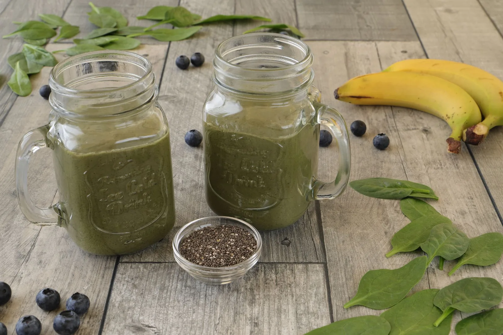 Zeleni smoothie sa spanaćem i jagodama u staklenoj čaši sa slamčicom i svežim sastojcima